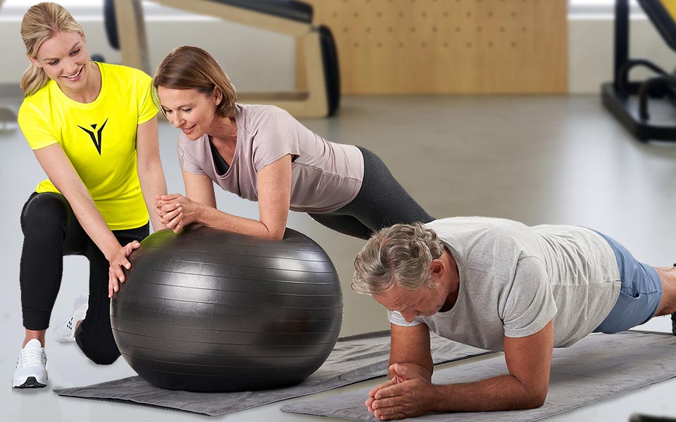 Eine Trainerin macht mit zwei Kunden Kraftaufbautraining im Gesundheitsstudio