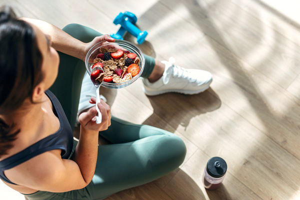 Eine Frau in sportlichem Outfit hält eine gesunde Schüssel Müsli mit Obst — jetzt über Stressbewältigung am Arbeitsplatz informieren!